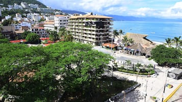 Un hôtel à plusieurs étages doté de balcons, une plage avec une structure en chaume, et une vue sur la mer.
