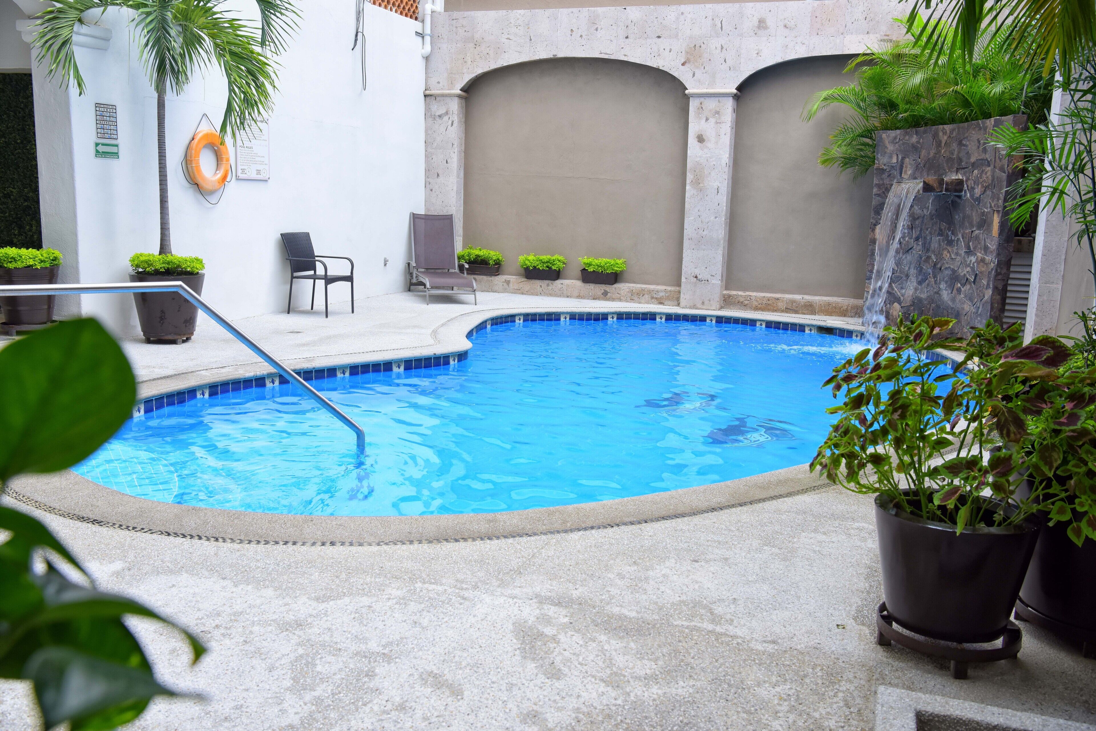 A swimming pool with a stone wall, potted plants, and a chair.