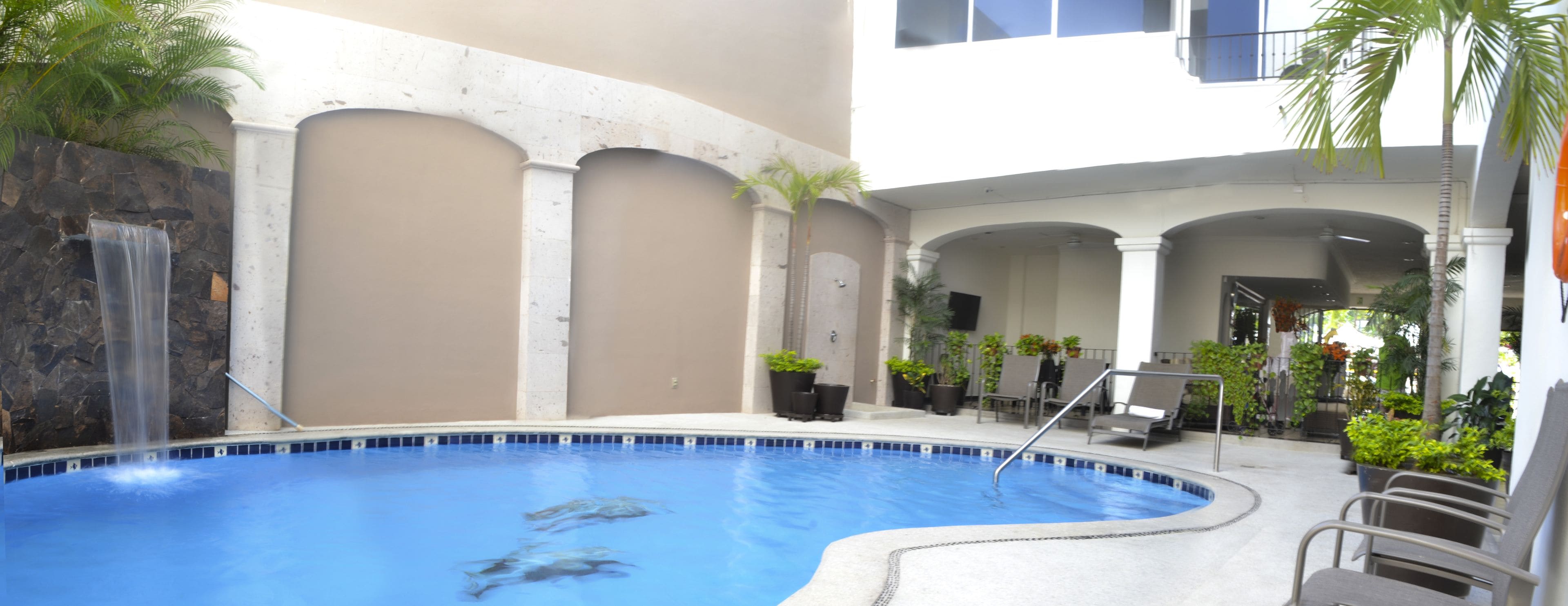 Una piscina con una cascada, rodeada de sillas de descanso y plantas en macetas.