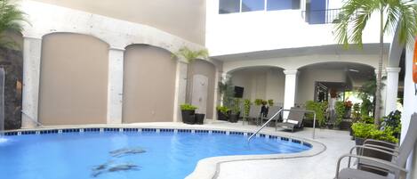 Una piscina con una cascada, rodeada de sillas de descanso y plantas en macetas.