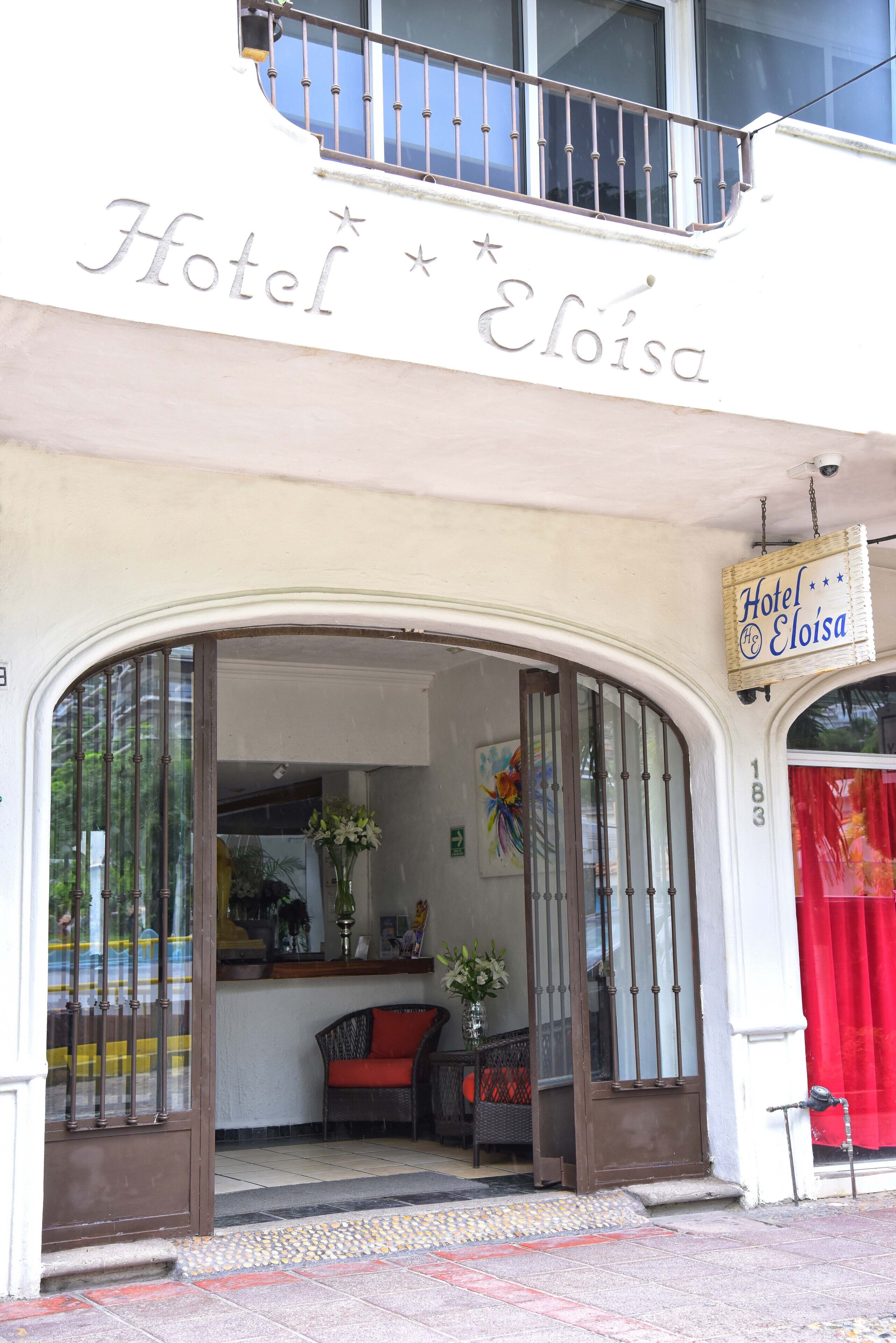 L’hôtel Eloisa, avec une enseigne au-dessus de l’entrée, un rideau rouge et une chaise avec un coussin rouge à l’intérieur.