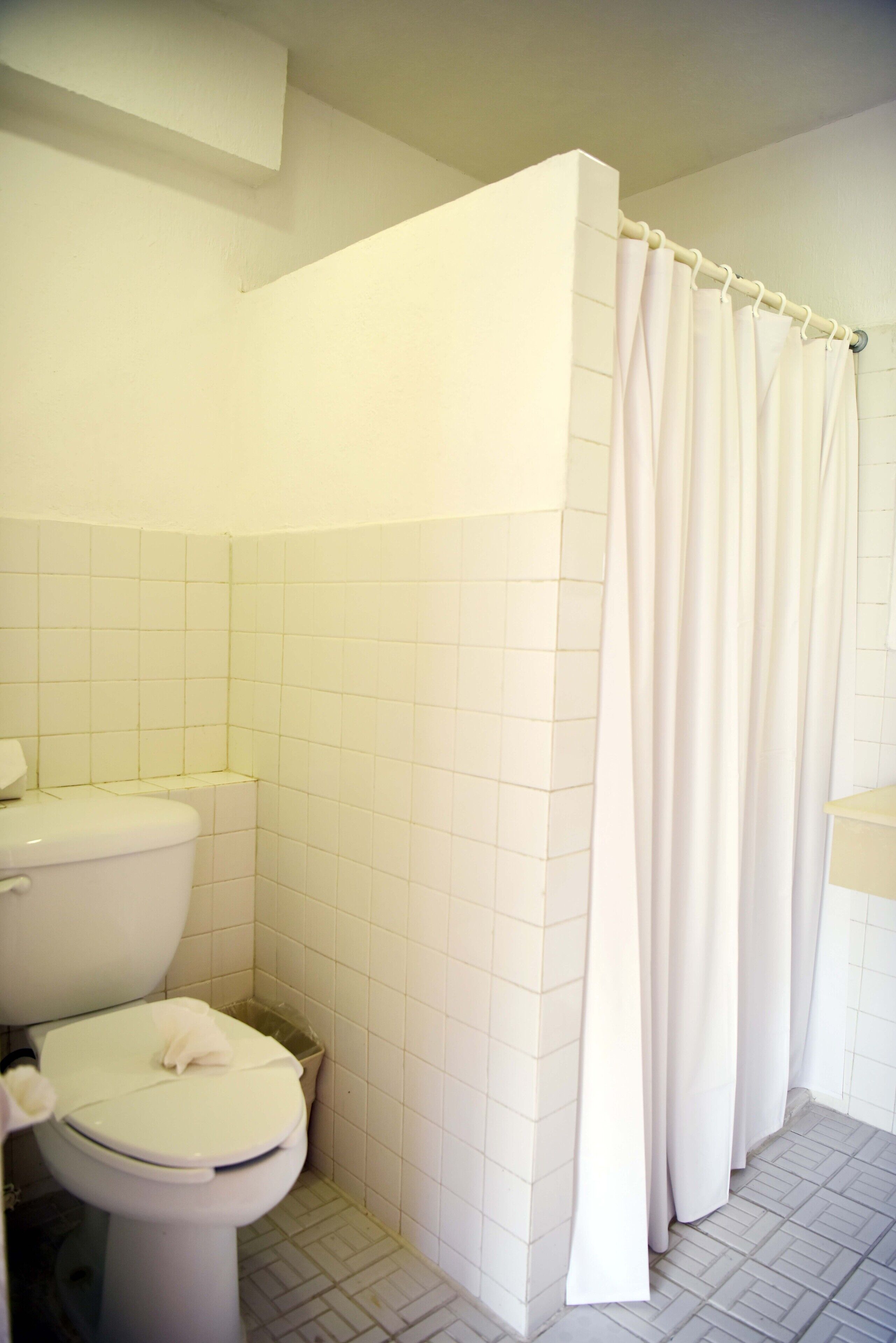 Une salle de bain avec des toilettes, un rideau de douche et des murs carrelés.