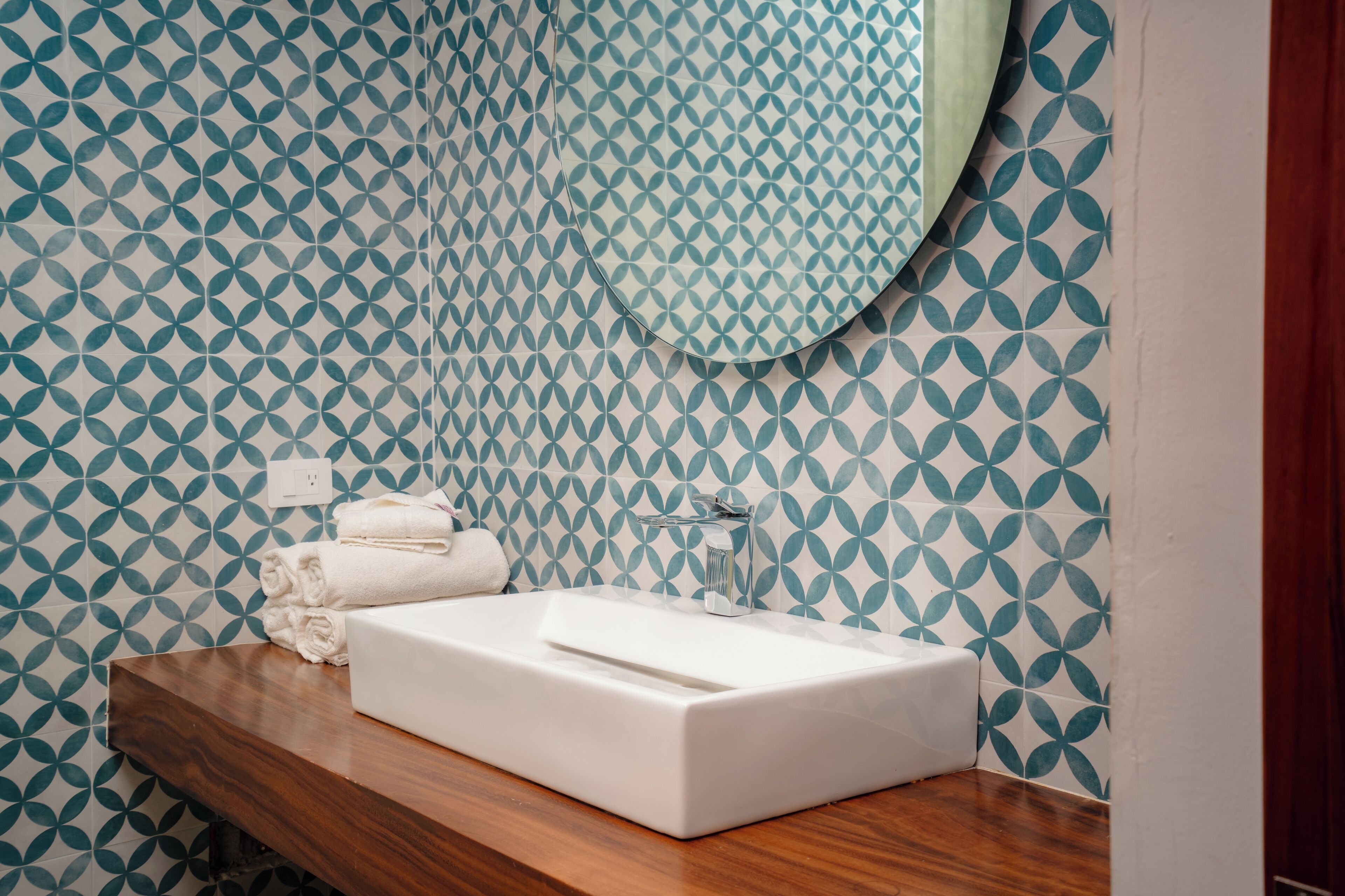 A bathroom with a white sink, wooden countertop, and patterned wall tiles.