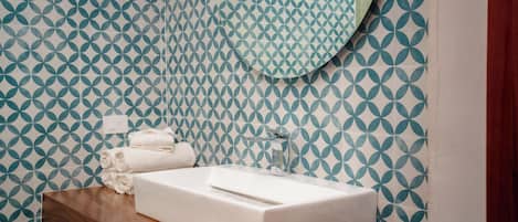 A bathroom with a white sink, wooden countertop, and patterned wall tiles.