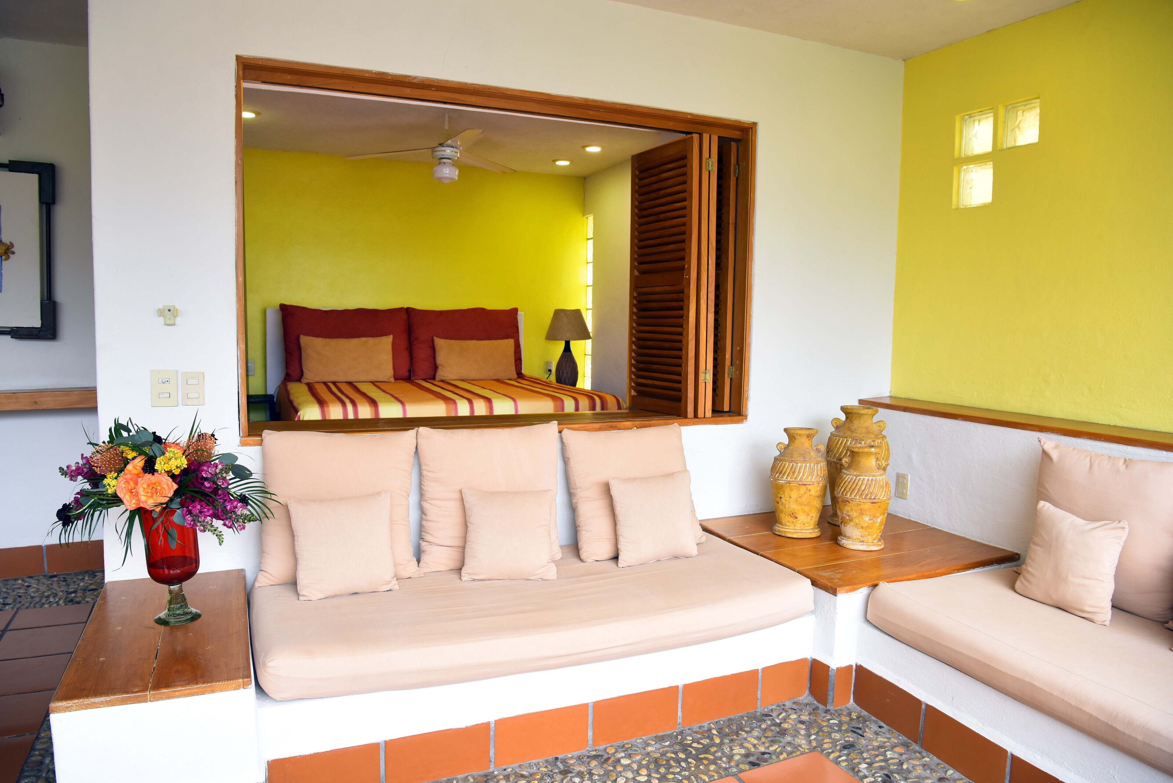 A room with a sofa, a table with a vase of flowers, and a bed with a striped blanket.