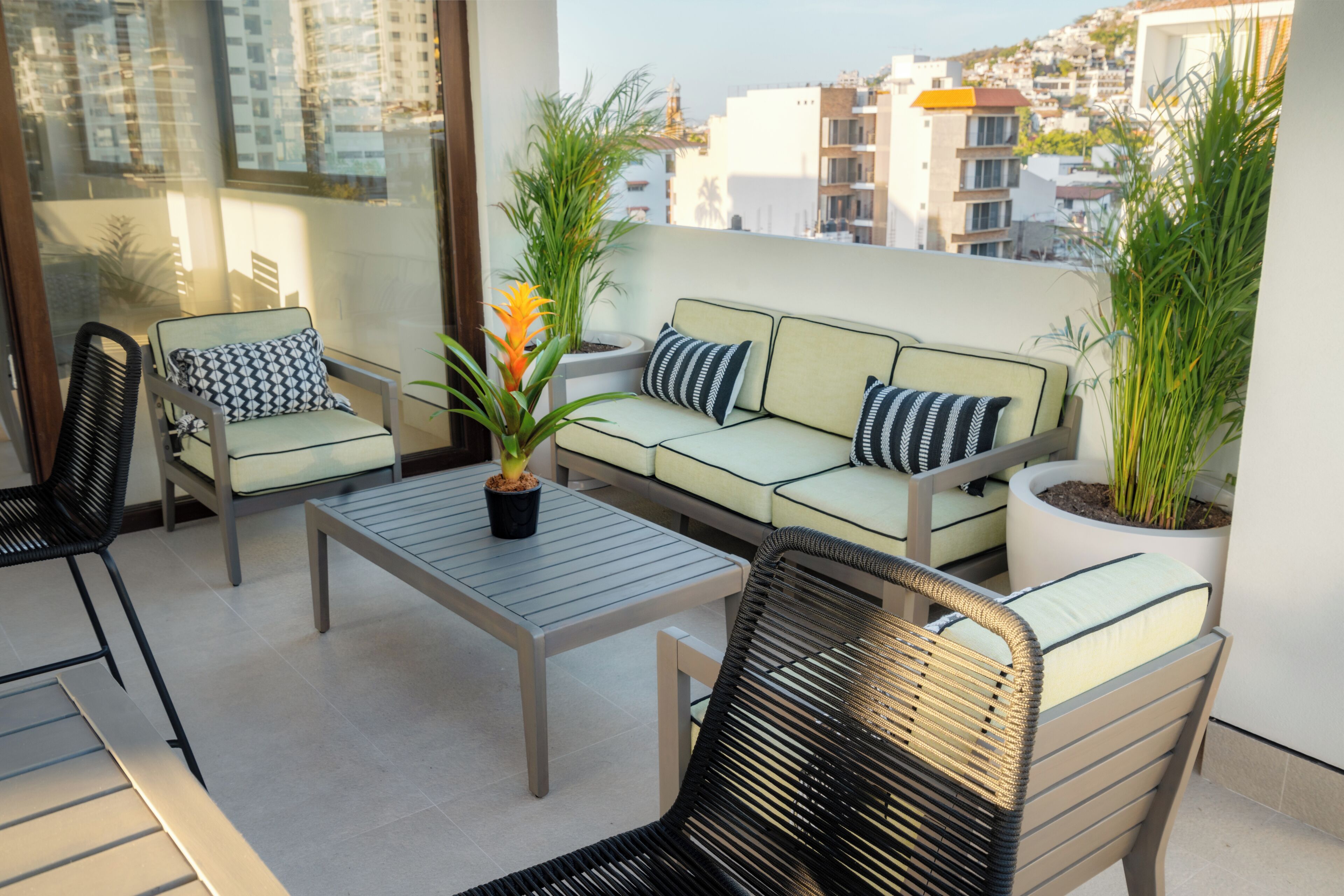 Een balkon met een bank, stoelen, een tafel en plantenpotten.