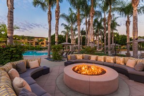 A poolside area with a circular fire pit surrounded by a curved seating area with striped cushions. - MarBrisa Carlsbad Resort (Carlsbad)