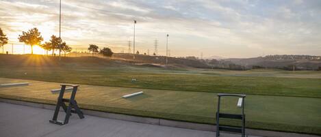 A golf course with a clear sky, a sunset, and a few benches along the edge.