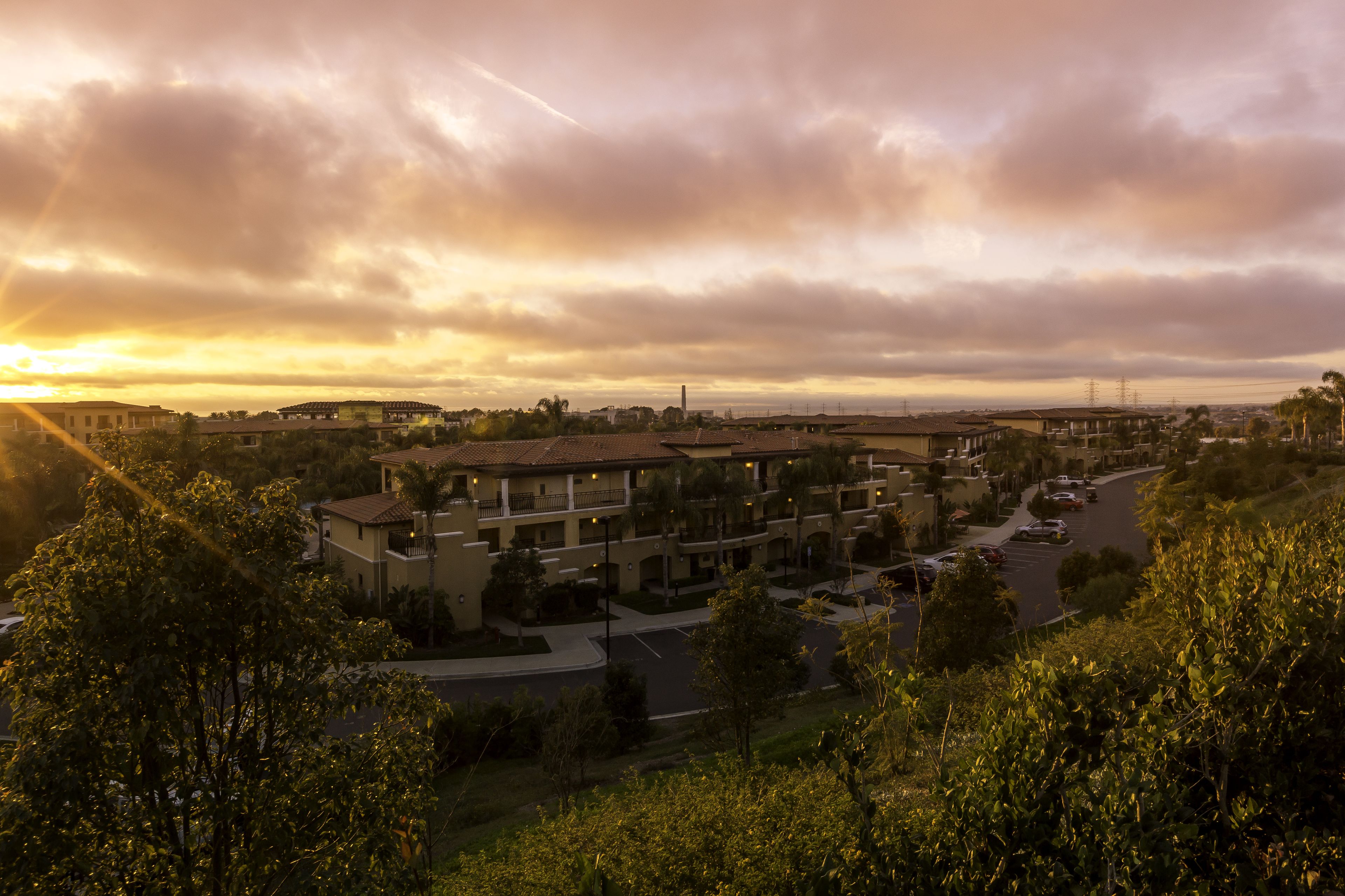 A residential area with multiple-story buildings, a parking lot, and a clear view of the sunset.