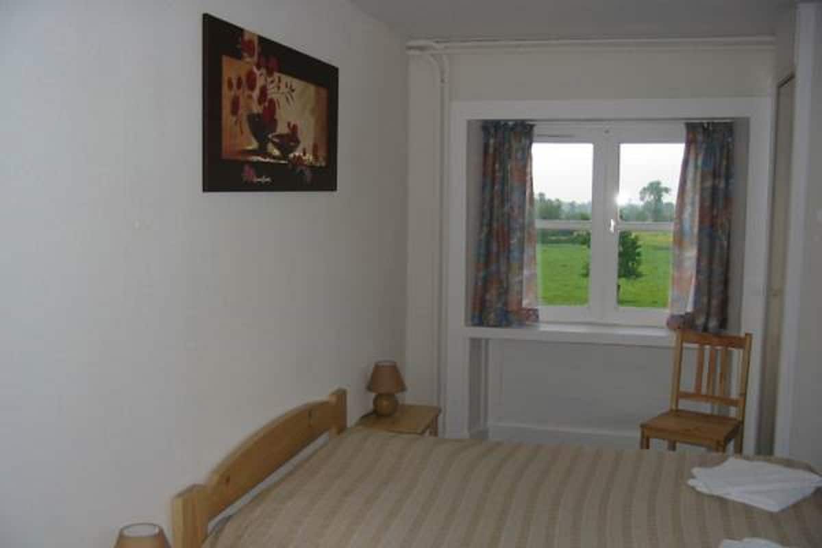 Une chambre à coucher avec un lit, deux tables de chevet, une chaise, une fenêtre avec des rideaux et un tableau au mur.