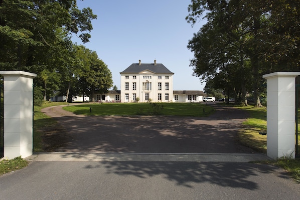 Un grand bâtiment symétrique, doté d’une entrée centrale, entouré d’une pelouse bien entretenue et d’arbres.