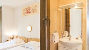 A hotel room with two beds, a bathroom with a sink and mirror, and a wall-mounted picture. - Ma Normandie by Popinns (Breville-les-Monts)