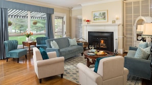A cozy living room with a fireplace, comfortable seating, and a view of the outdoors. - The Four Chimneys Inn (Bennington)