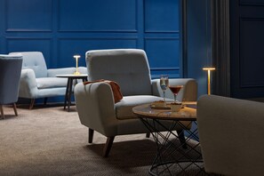 A room with a blue wall, a grey armchair, a round table, and a small side table with a lamp.