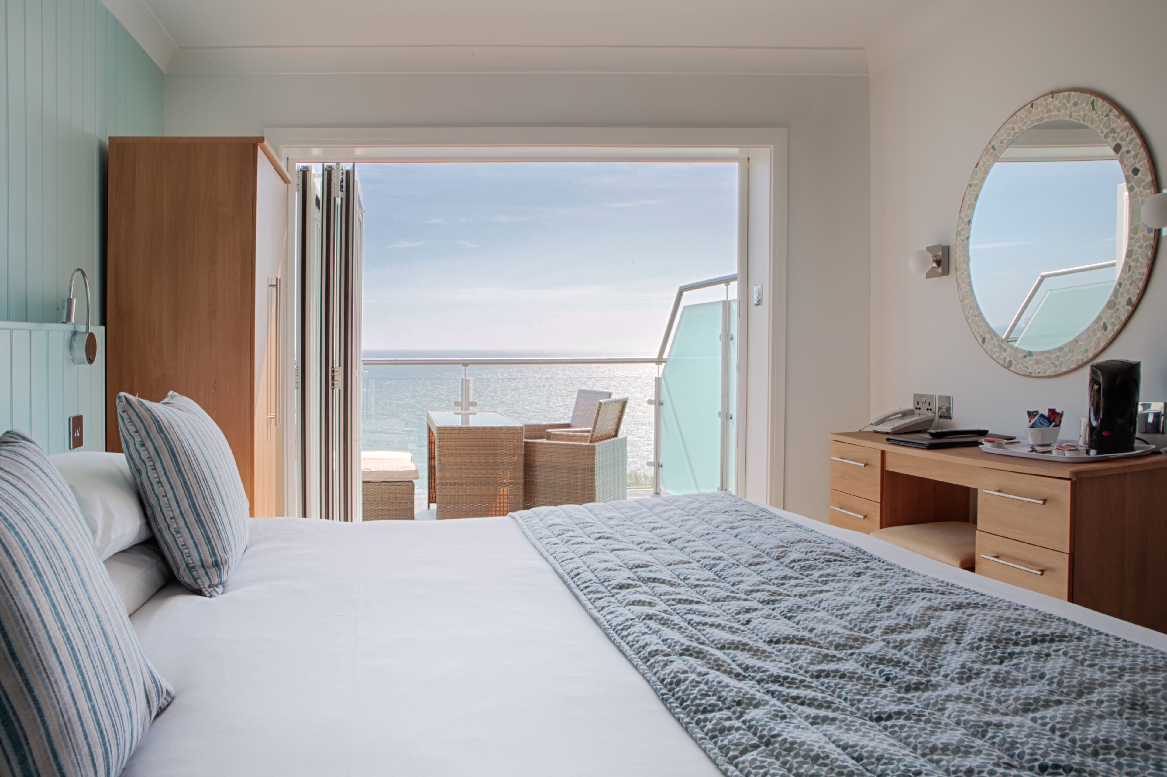 Un dormitorio con cama, escritorio, silla y balcón con vista al mar.