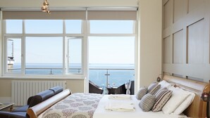 A bedroom with a large window, a bed with pillows, a bedside table, and a chair. - Luccombe Hall Hotel (Shanklin)