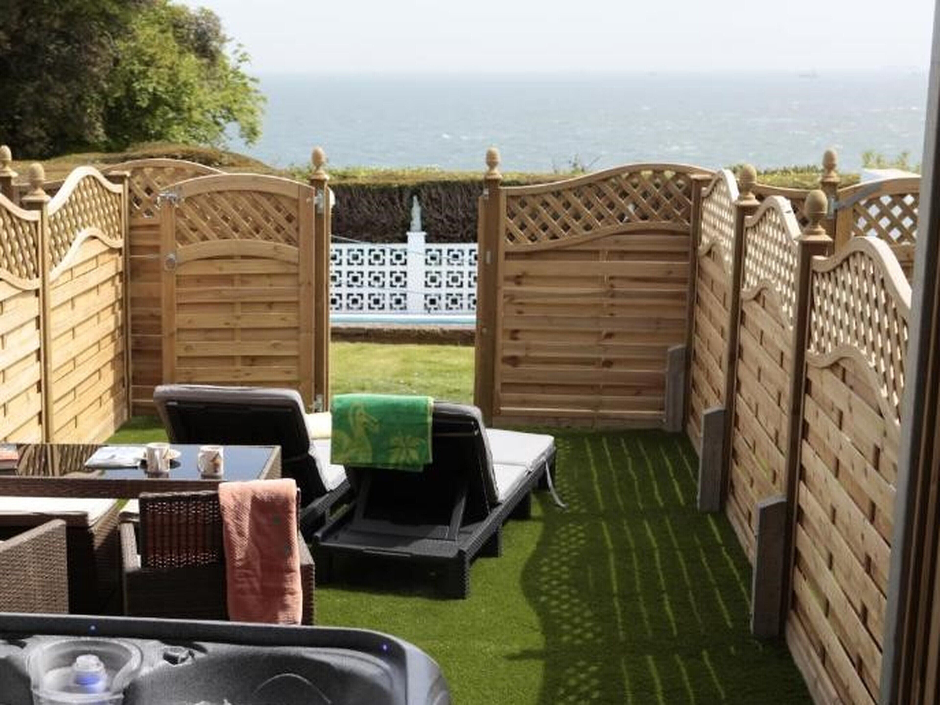 A patio area with a view of the sea, wooden fences, and outdoor furniture.