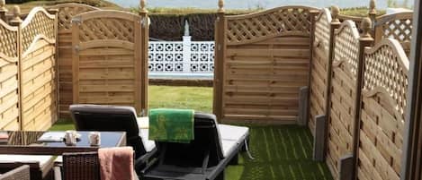 A patio area with a view of the sea, wooden fences, and outdoor furniture.