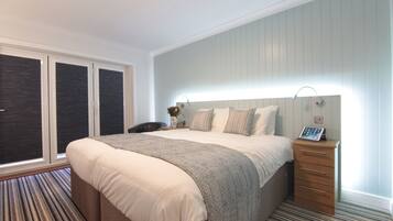 A bedroom with a large bed, a bedside table with a lamp, a chair, and a window with blinds.