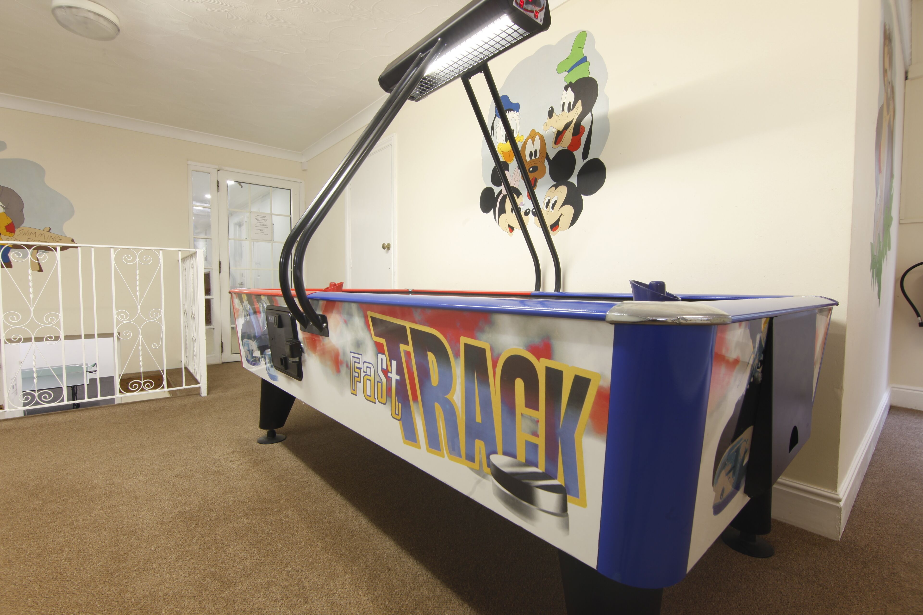 A room with a play area featuring a 'Fast Track' arcade machine, a white crib, and a wall with cartoon characters.