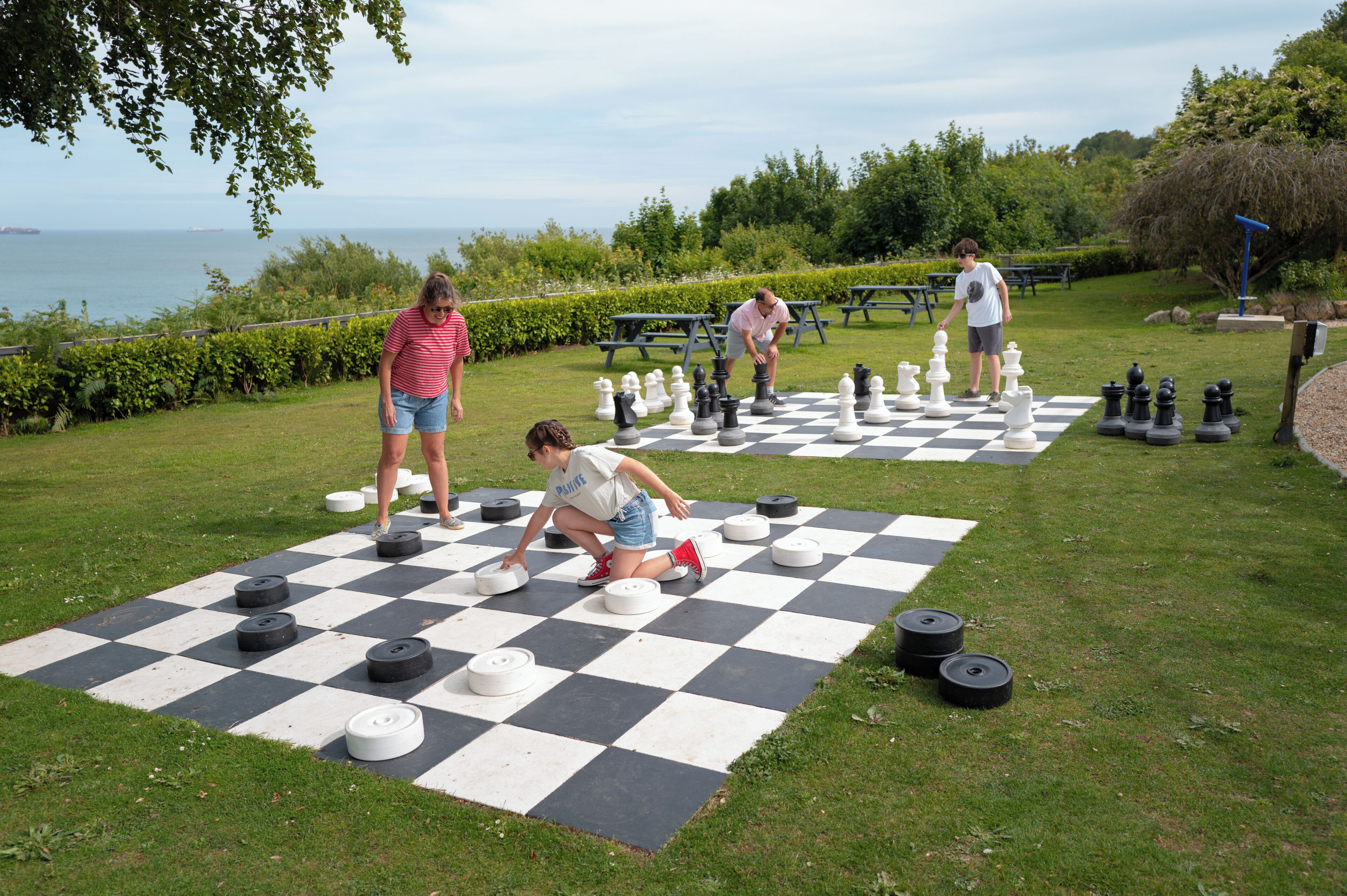 A checkered outdoor game area with picnic tables and a view of the sea.
