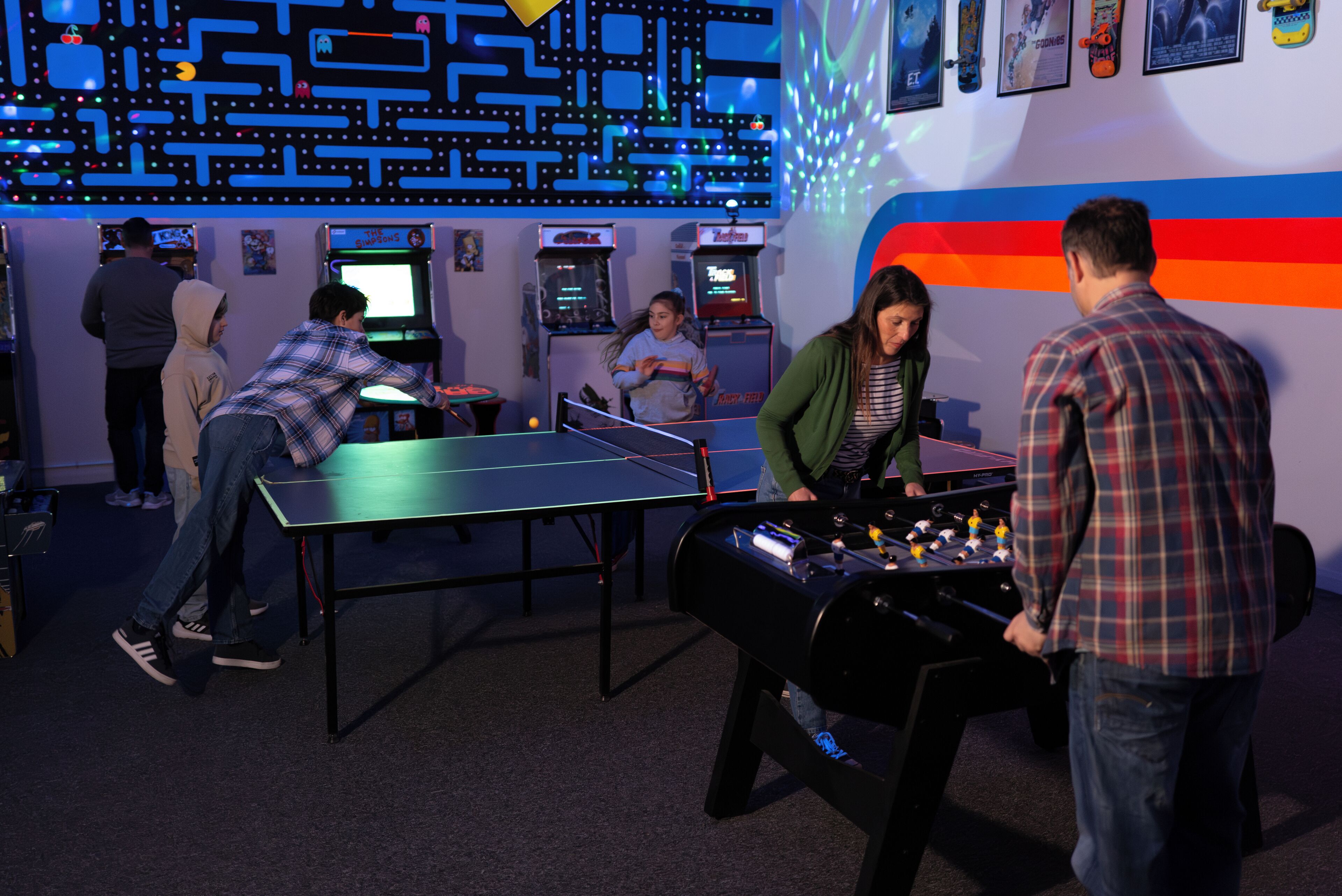 A room with a foosball table, arcade games, and a neon-lit wall.
