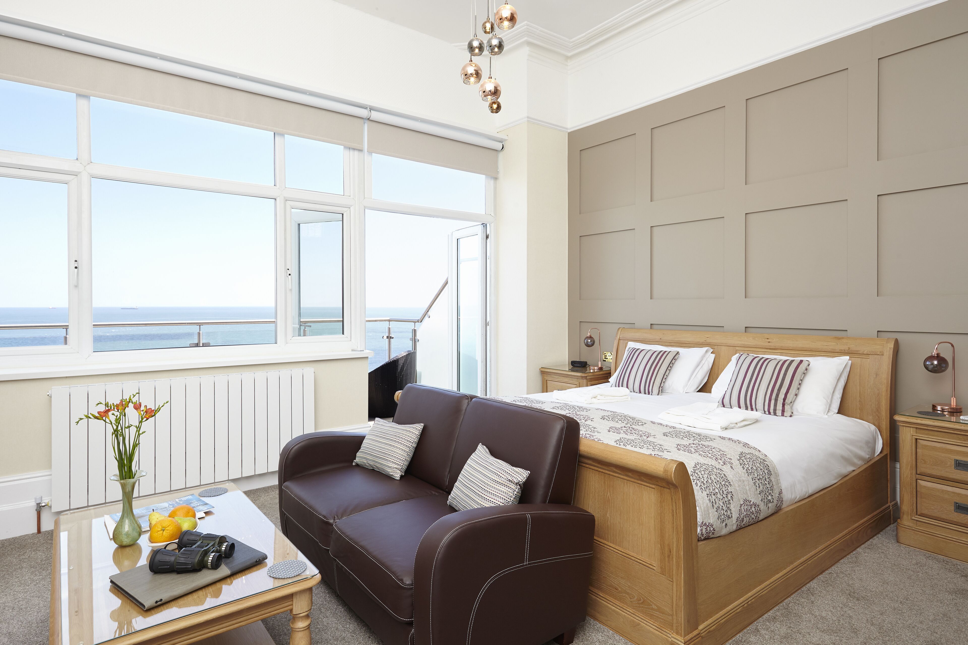 A bedroom with a bed, a sofa, a coffee table, and a view of the sea.