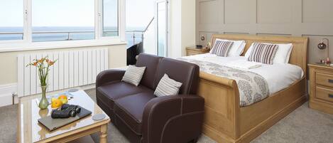 A bedroom with a bed, a sofa, a coffee table, and a view of the sea.