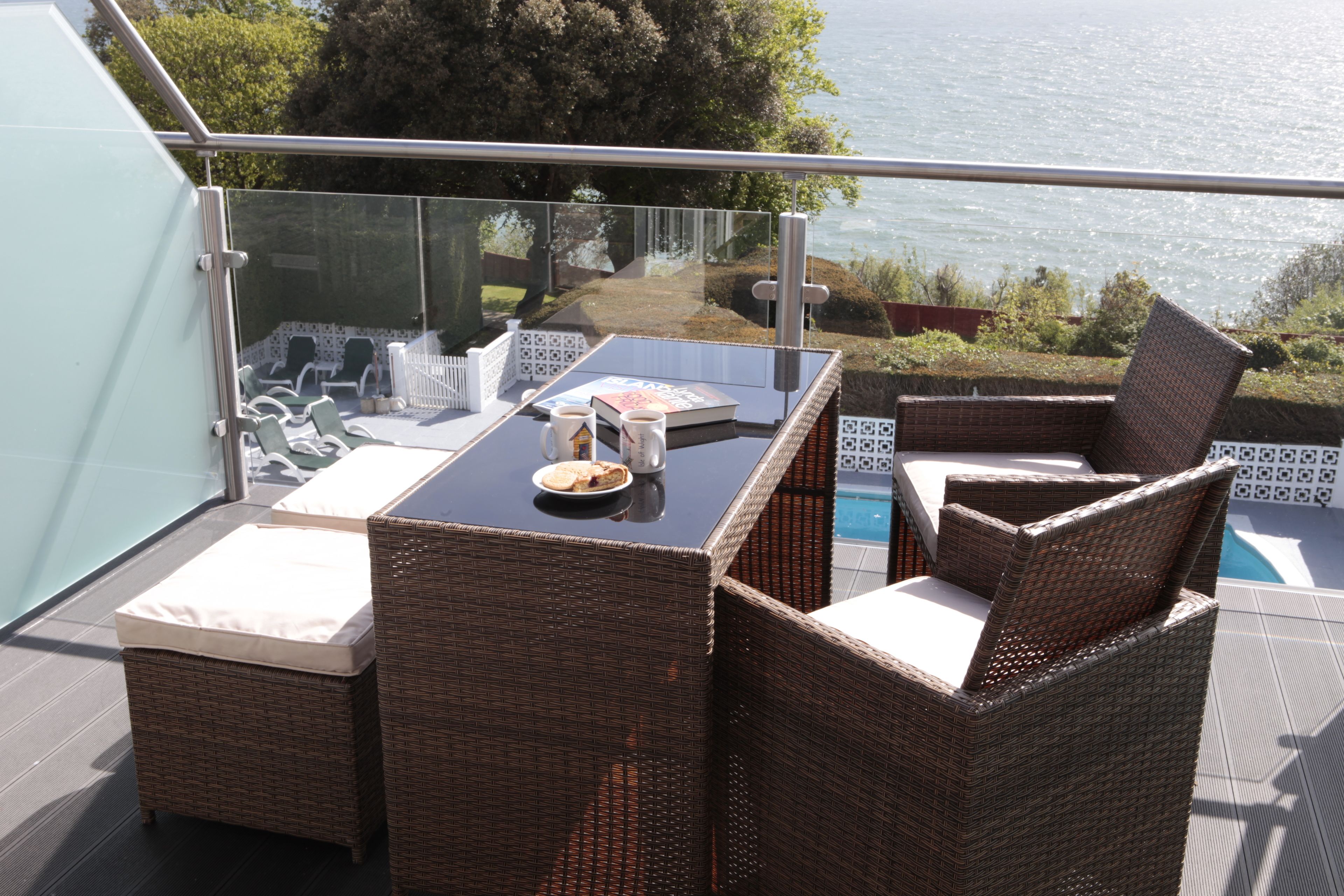 A balcony with wicker furniture, a glass table, and a view of the sea.
