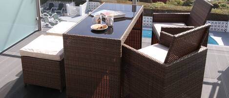 A balcony with wicker furniture, a glass table, and a view of the sea.