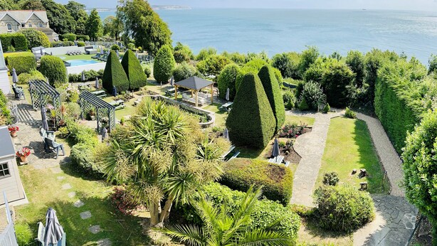 A landscaped garden with a pool, seating areas, and a gazebo overlooking a body of water. - Luccombe Hall Hotel (Shanklin)