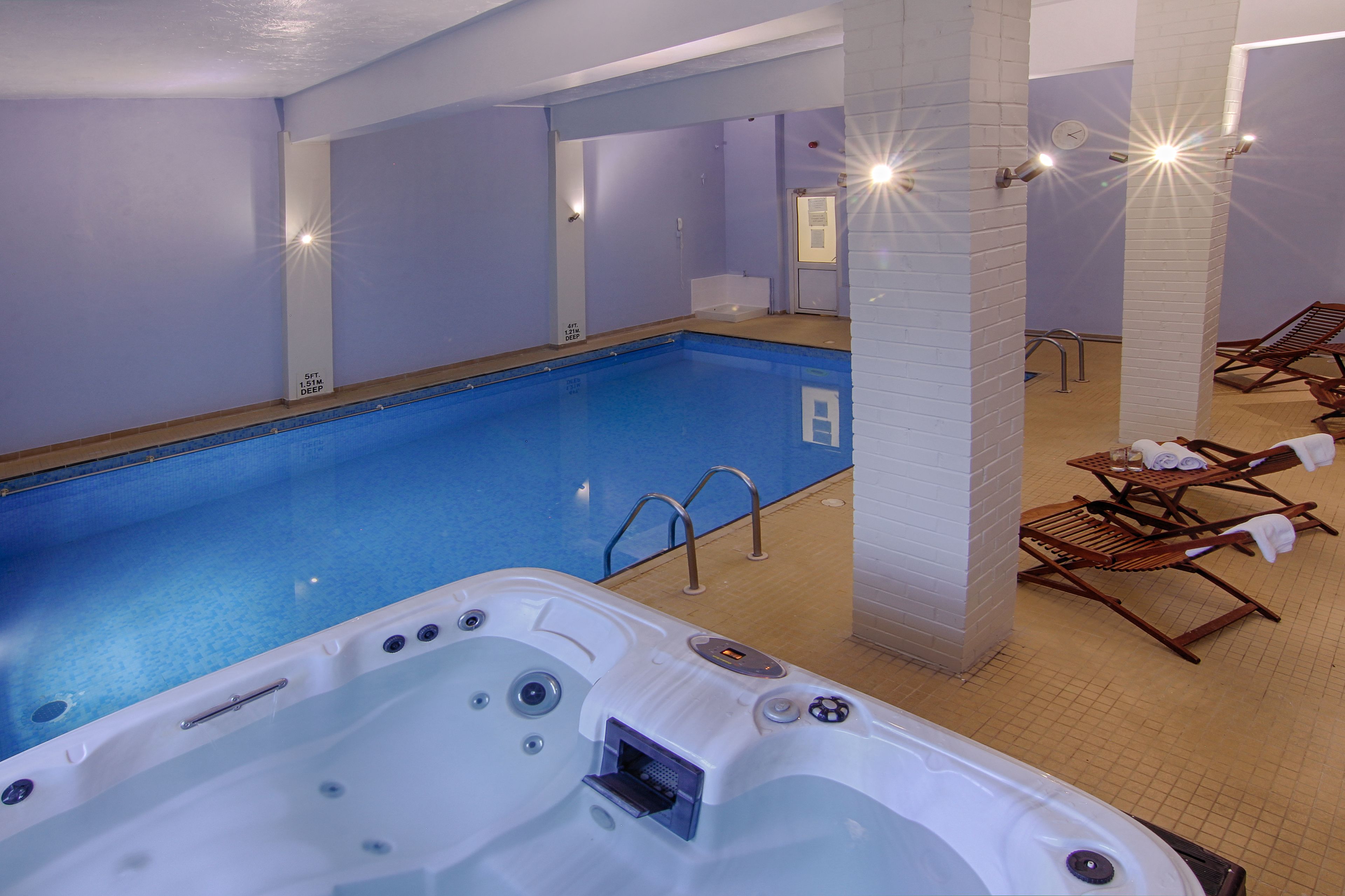 A swimming pool with a hot tub, lounge chairs, and a sunlit ceiling.