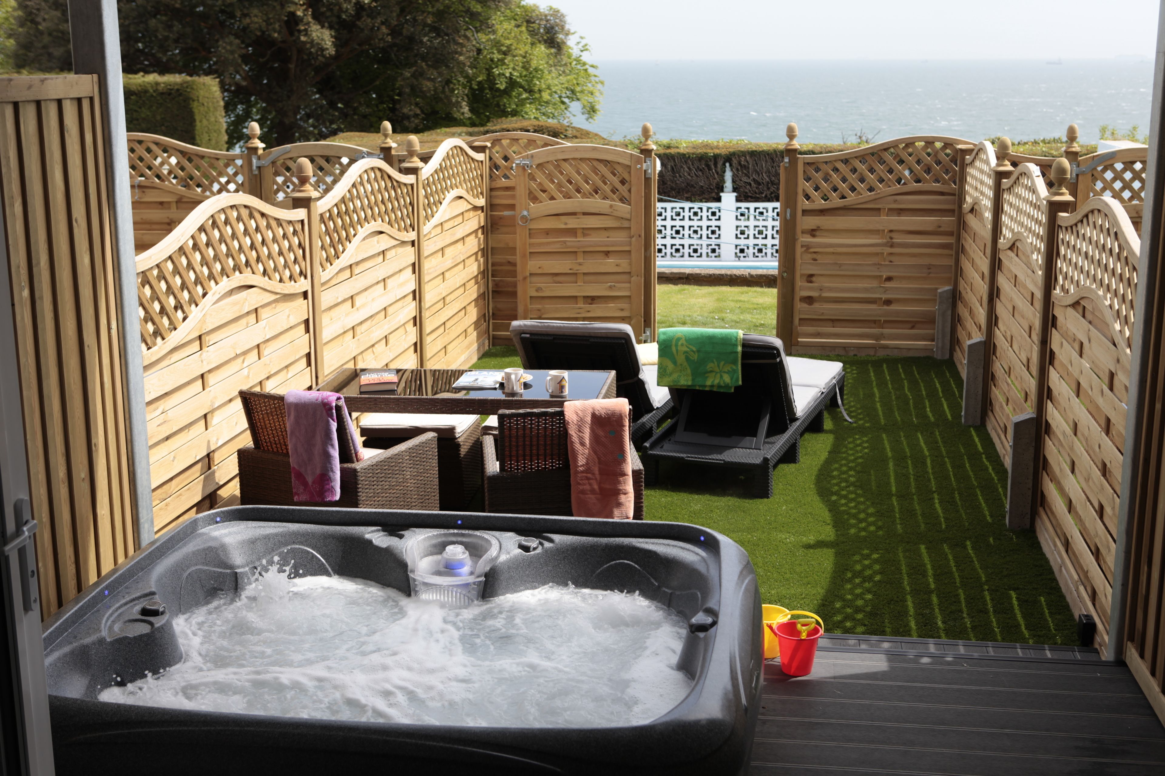 A hot tub with a view of the sea, surrounded by wooden fences and outdoor furniture.