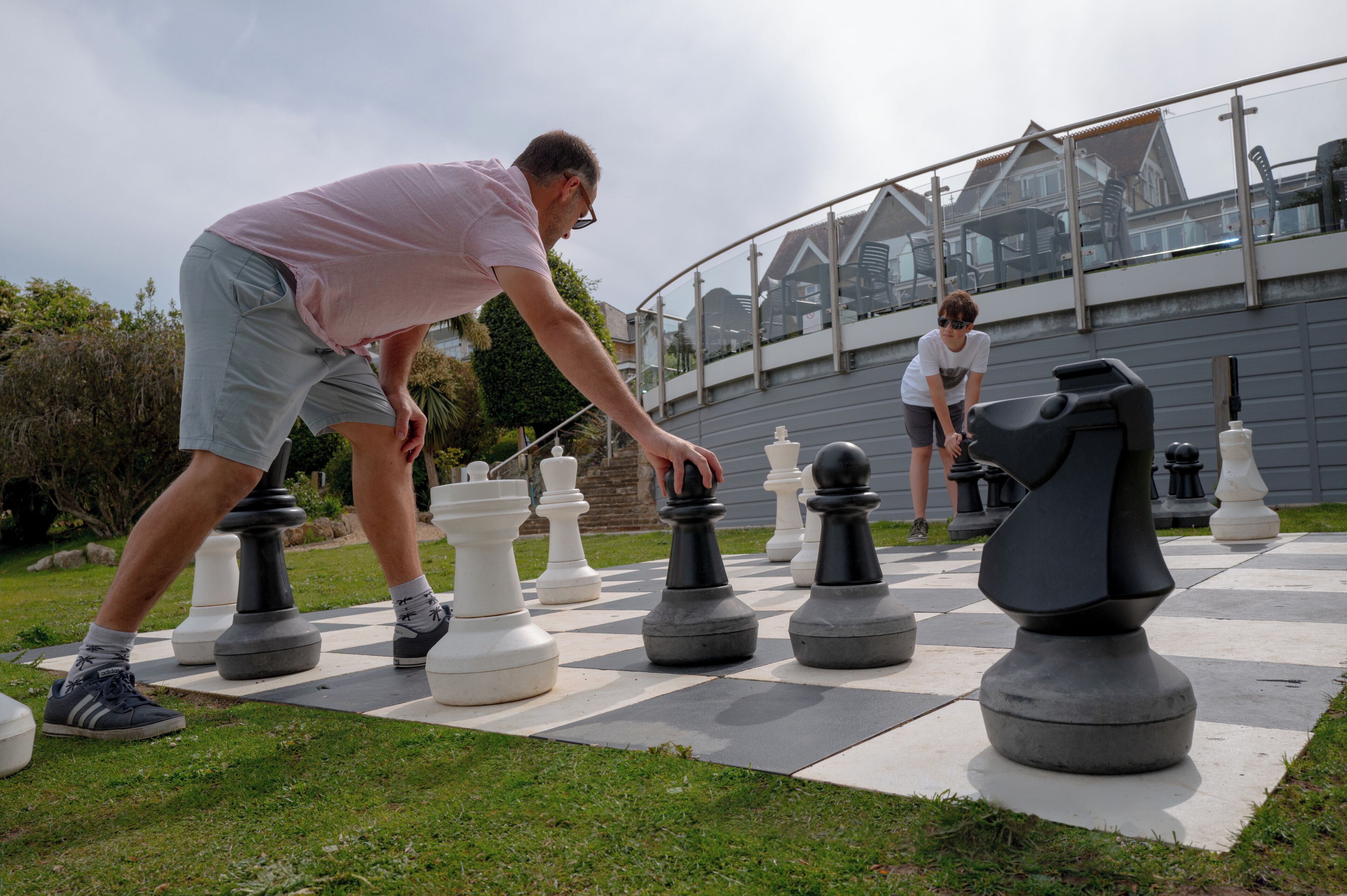 A chessboard with oversized pieces set up outdoors on a grassy area.