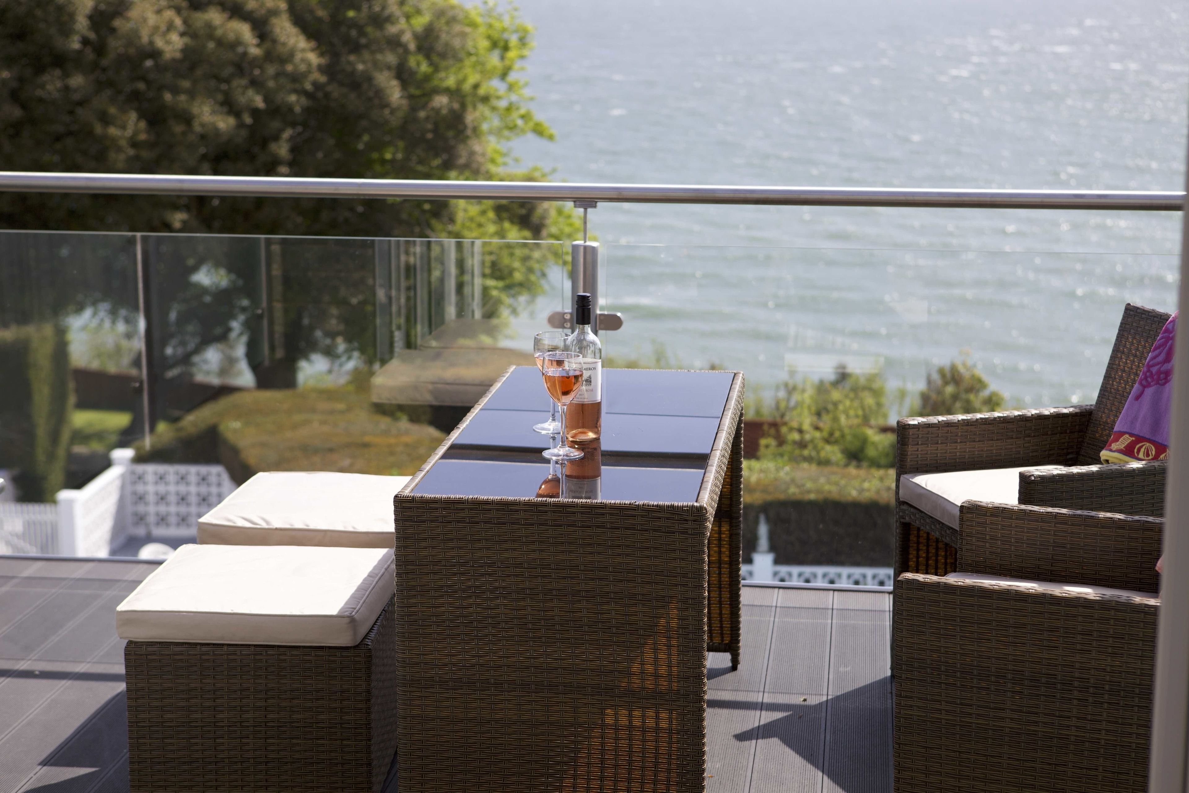 Un balcon agrémenté de meubles en osier, d’une table en verre et d’une bouteille de vin.