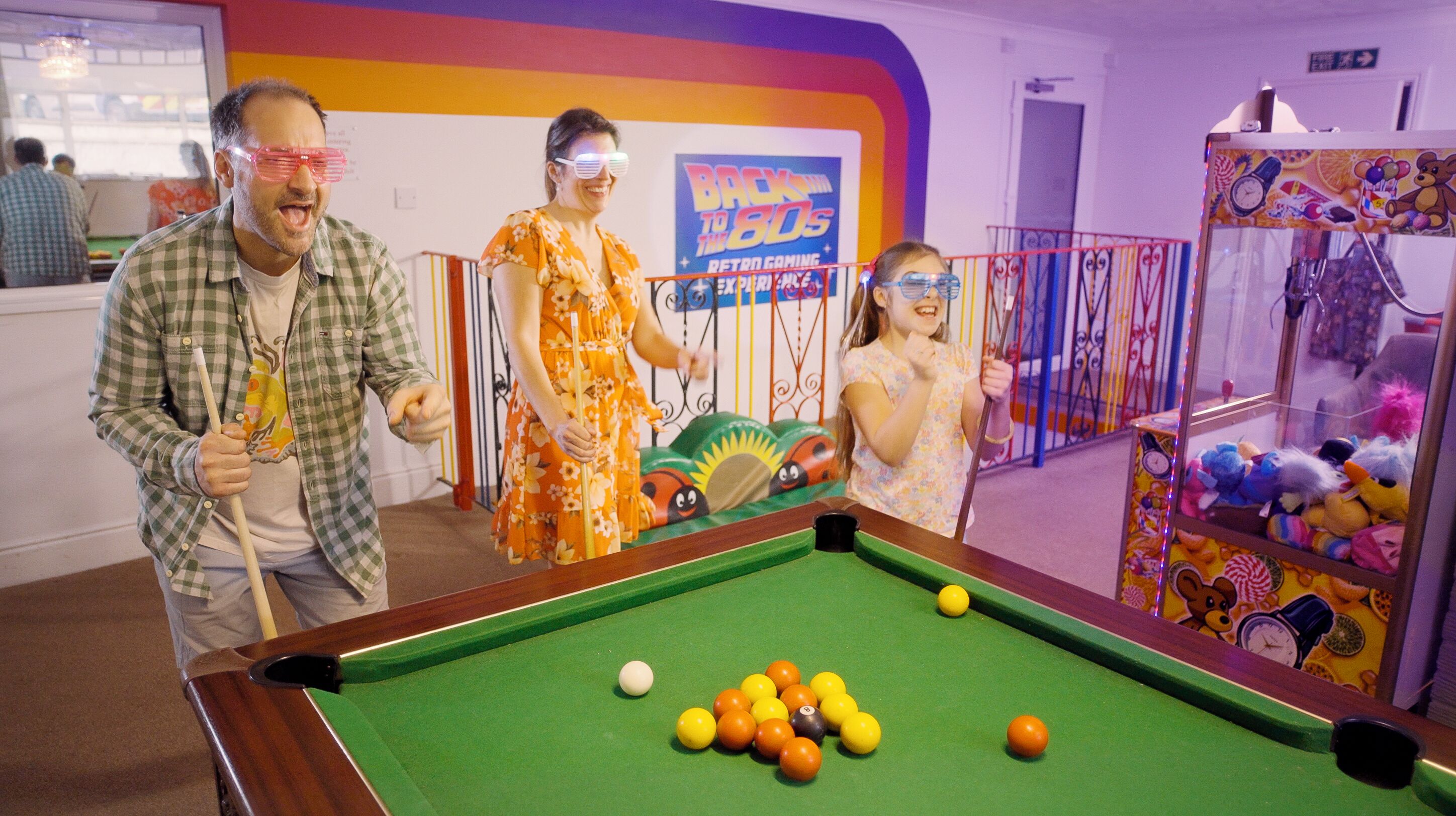 A pool table with balls, a claw machine, and a colorful wall with a 'Back to the 80s' sign.