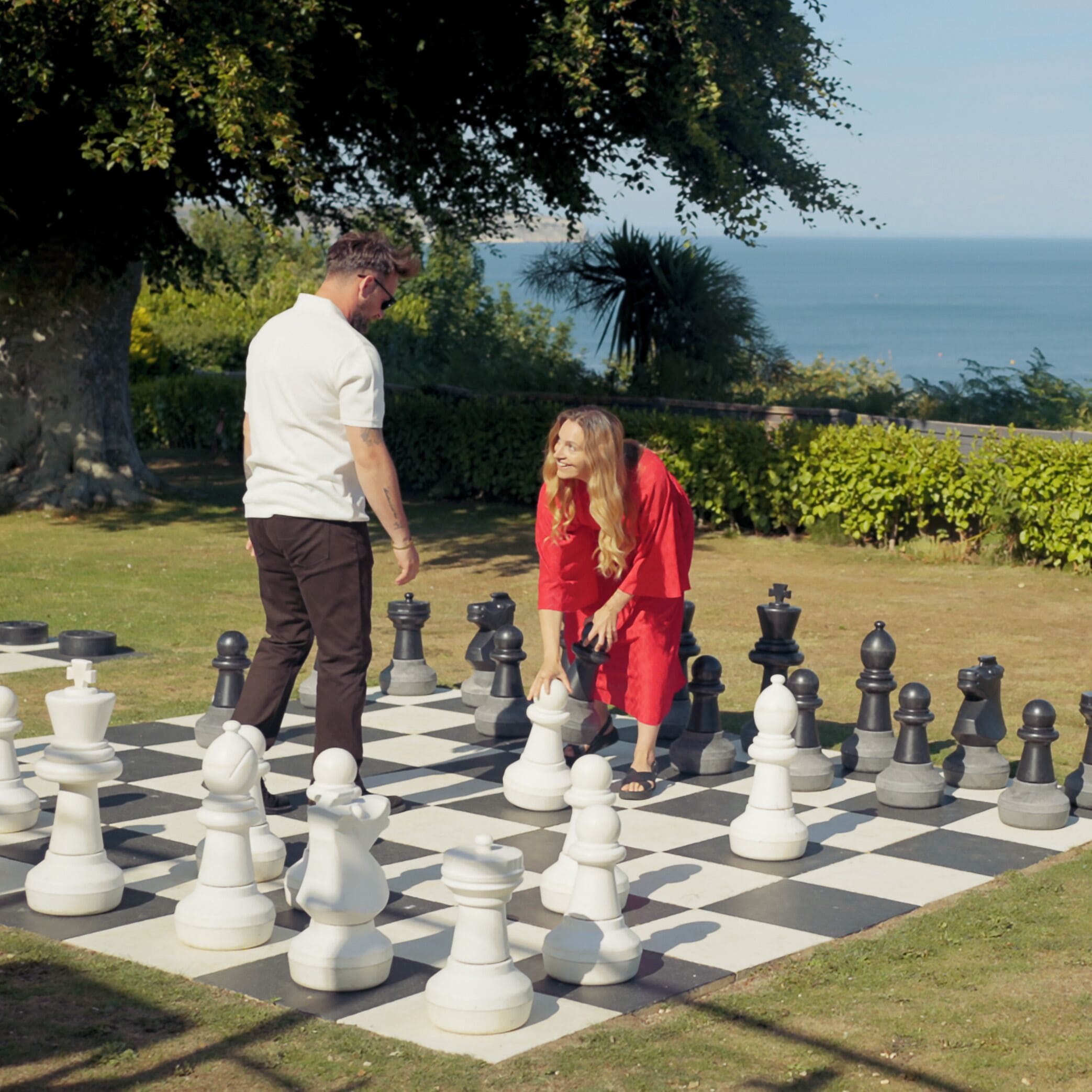A large outdoor chessboard with chess pieces, surrounded by grass and trees.