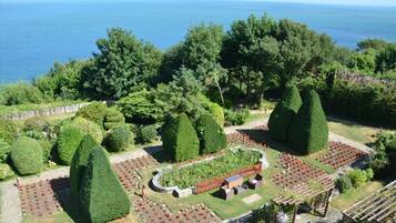Un jardín ajardinado con setos bien cuidados y una variedad de plantas, un espacio de descanso con bancos y vistas al mar.