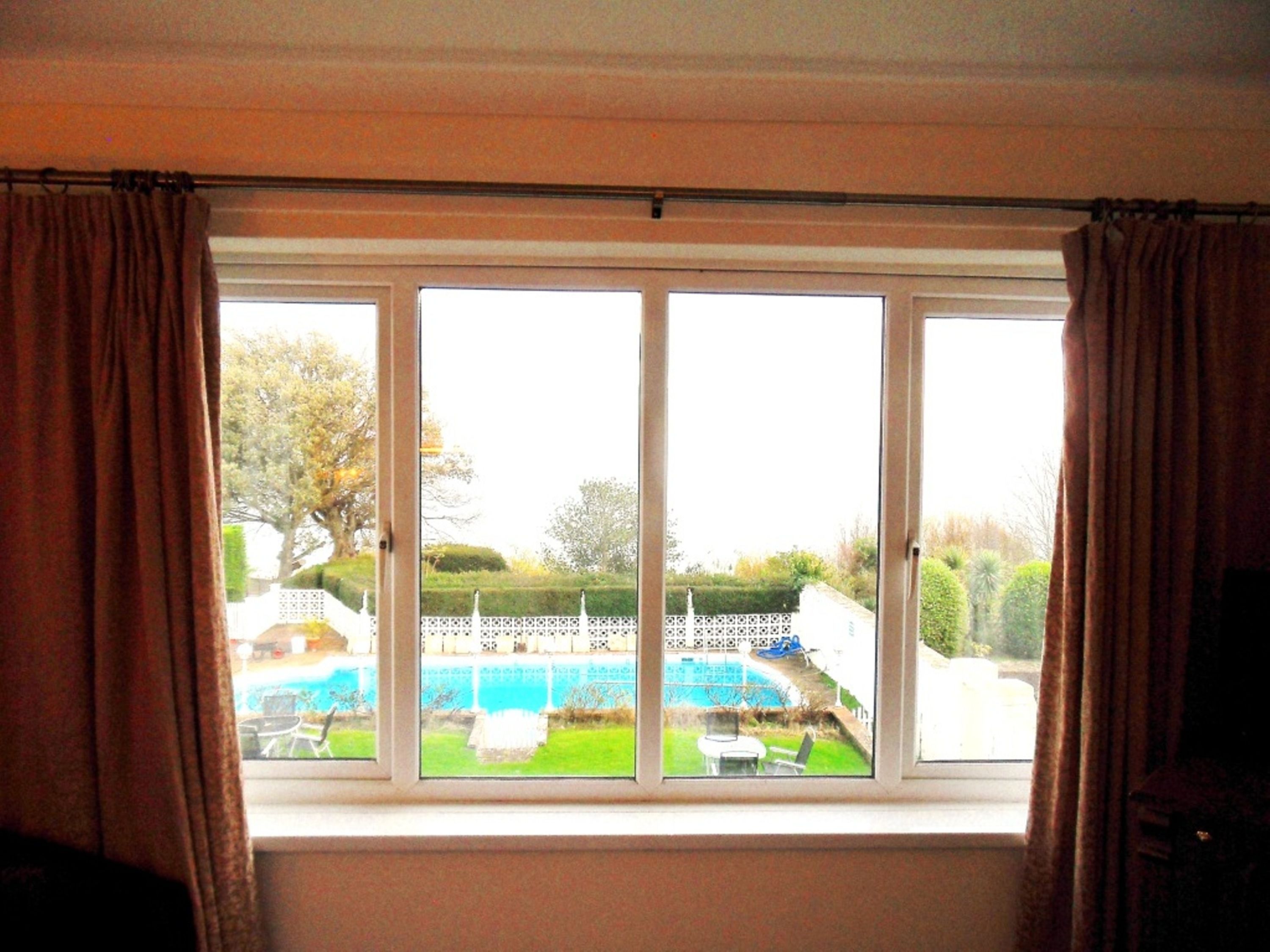 A room with a large window overlooking a swimming pool and a well-maintained garden.