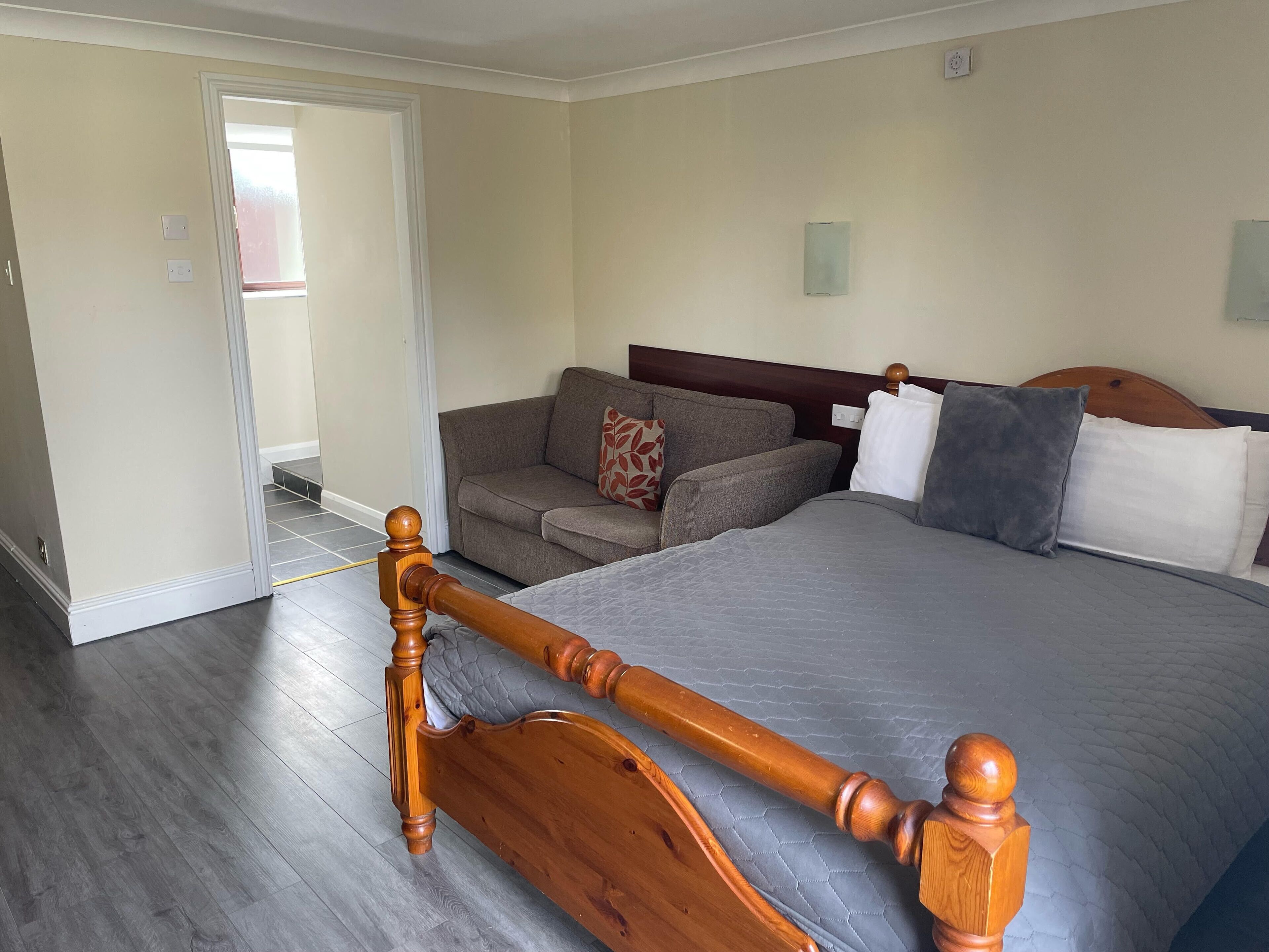 Ein Schlafzimmer mit einem hölzernen Bett, grauer Bettwäsche, einem grauen Sofa und einem Kissen mit Muster.