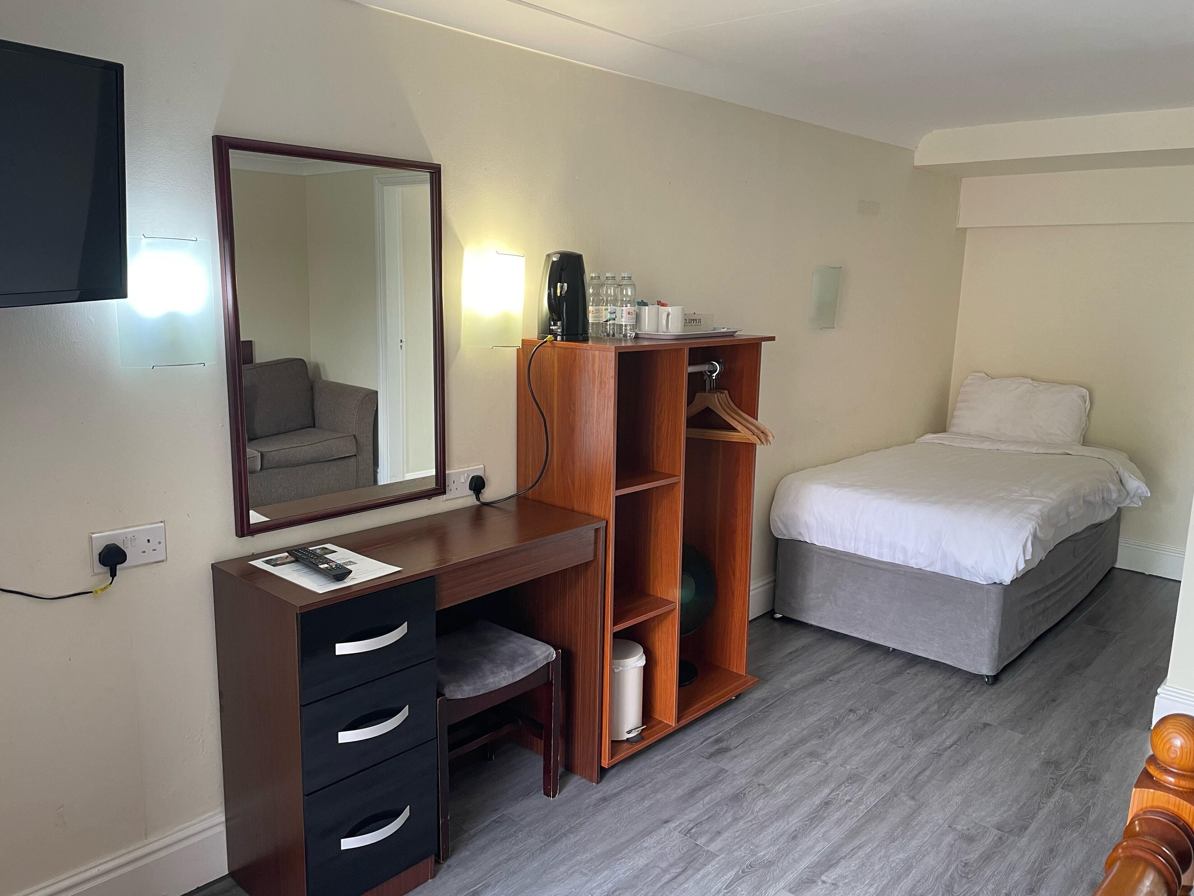 Una habitación de hotel con un escritorio de madera, una cama, un espejo y un armario.