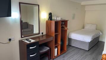 Una habitación de hotel con un escritorio de madera, una cama, un espejo y un armario.