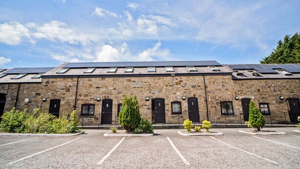A stone building with solar panels on the roof, a parking lot, and small trees in front. - Mountain Park Hotel (Flint)