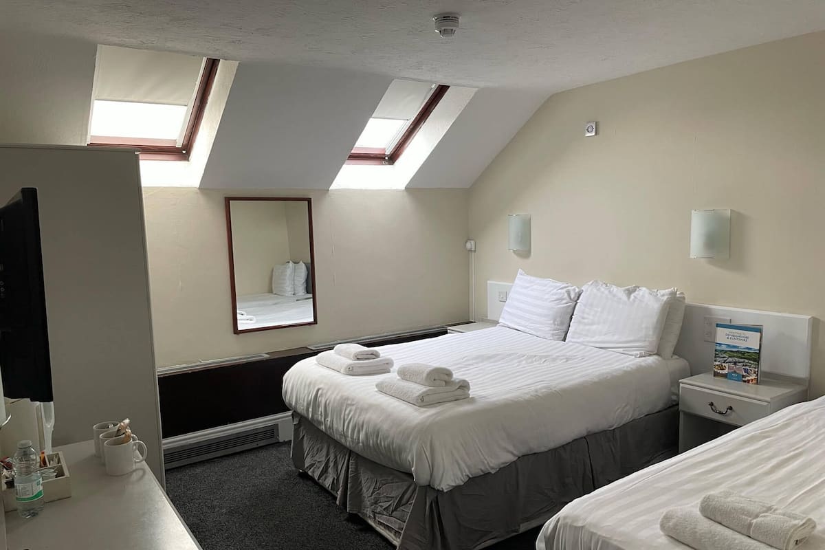 Hotellihuone, jossa on kaksi sänkyä, työpöytä tuolilla, peili ja kattovalokuvioita.