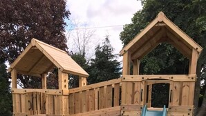 A wooden playground structure with a slide and climbing net. - Mountain Park Hotel (Flint)