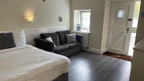 A room with a bed, a sofa, a window with blinds, a door, and a radiator. - Mountain Park Hotel (Flint)