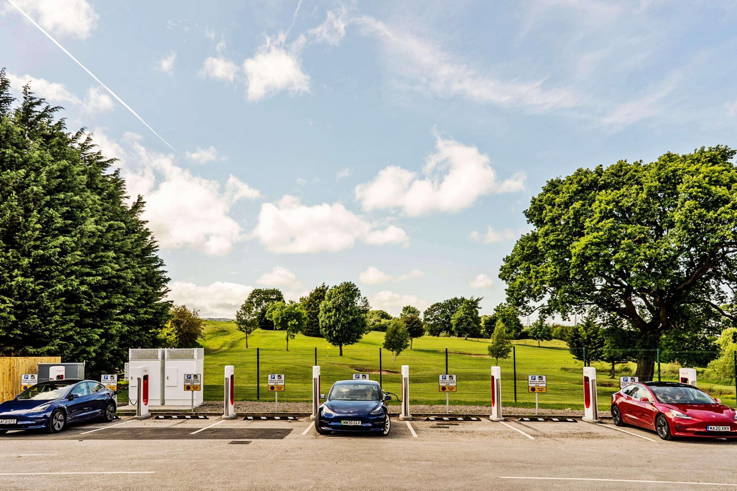 Een parkeerplaats met oplaadpunten voor elektrische voertuigen, een blauwe auto en een rode auto.