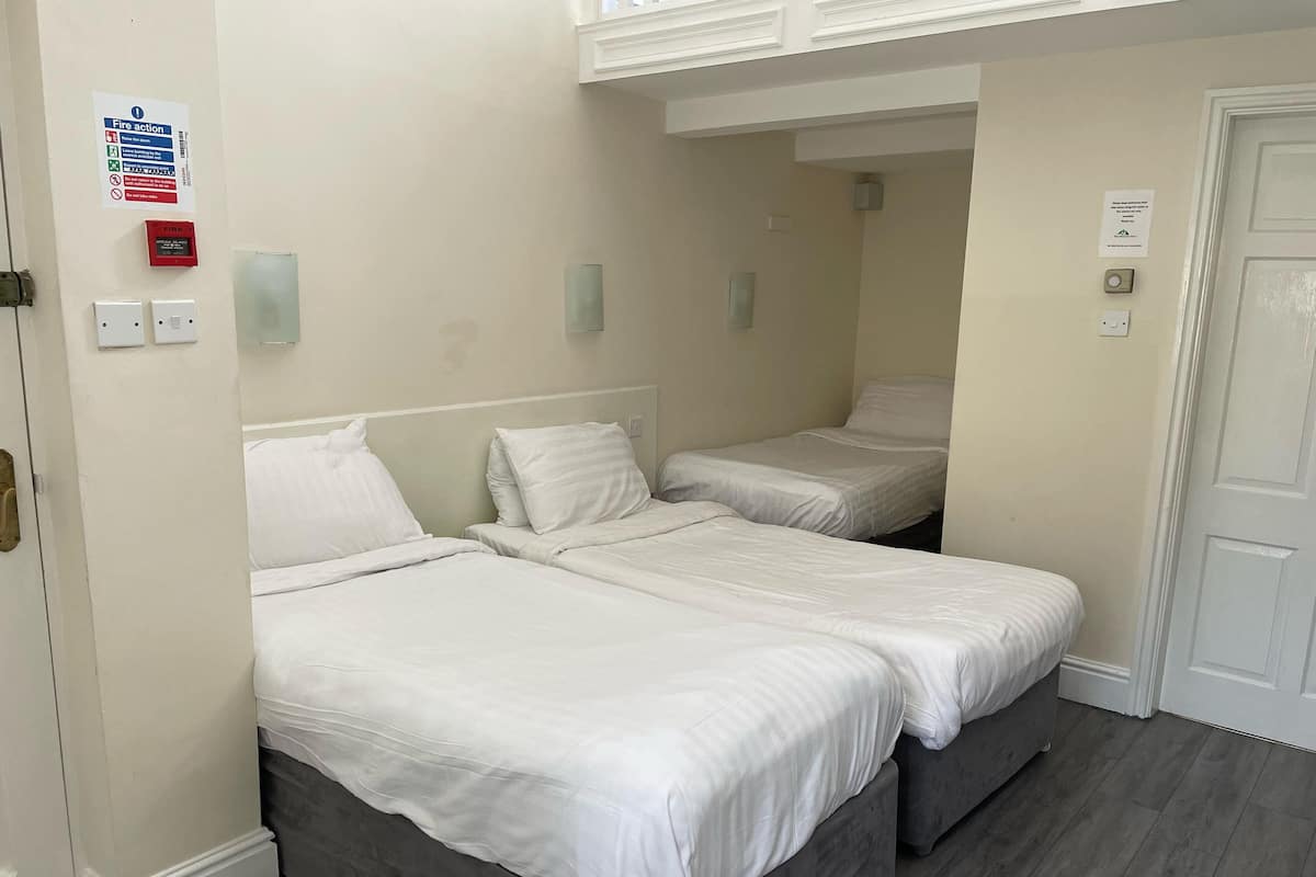 Hotellihuone, jossa on kaksi erillistä sänkyä, ovi, valokytkin ja seinällä paloturvallisuusohje.