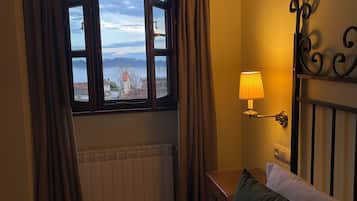 Een slaapkamer met een bed, nachtkastje, lamp, raam met gordijnen en uitzicht op water en gebouwen.