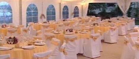 A tented event space with round tables, white tablecloths, and yellow sashes.